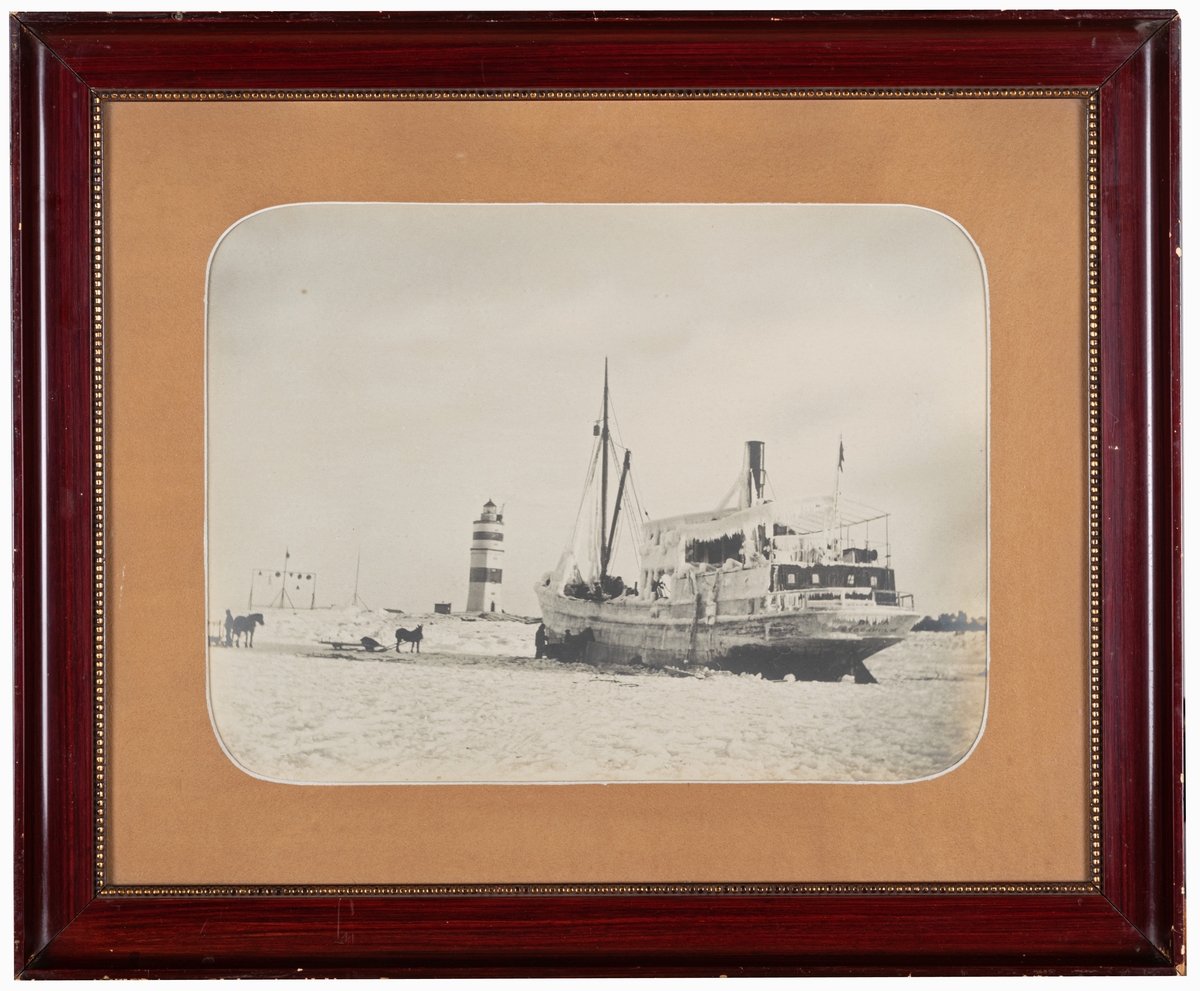 Foto. Frisat fartyg vid Örskärs fyr 1916. I brun profilerad ram och glas.
Mått:
a) foto 29x38cm.
b) ram 47x57cm.