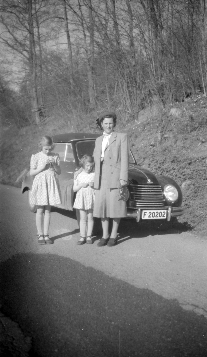 På vägen står en kvinna med två barn framför en parkerad bil, en DKW.