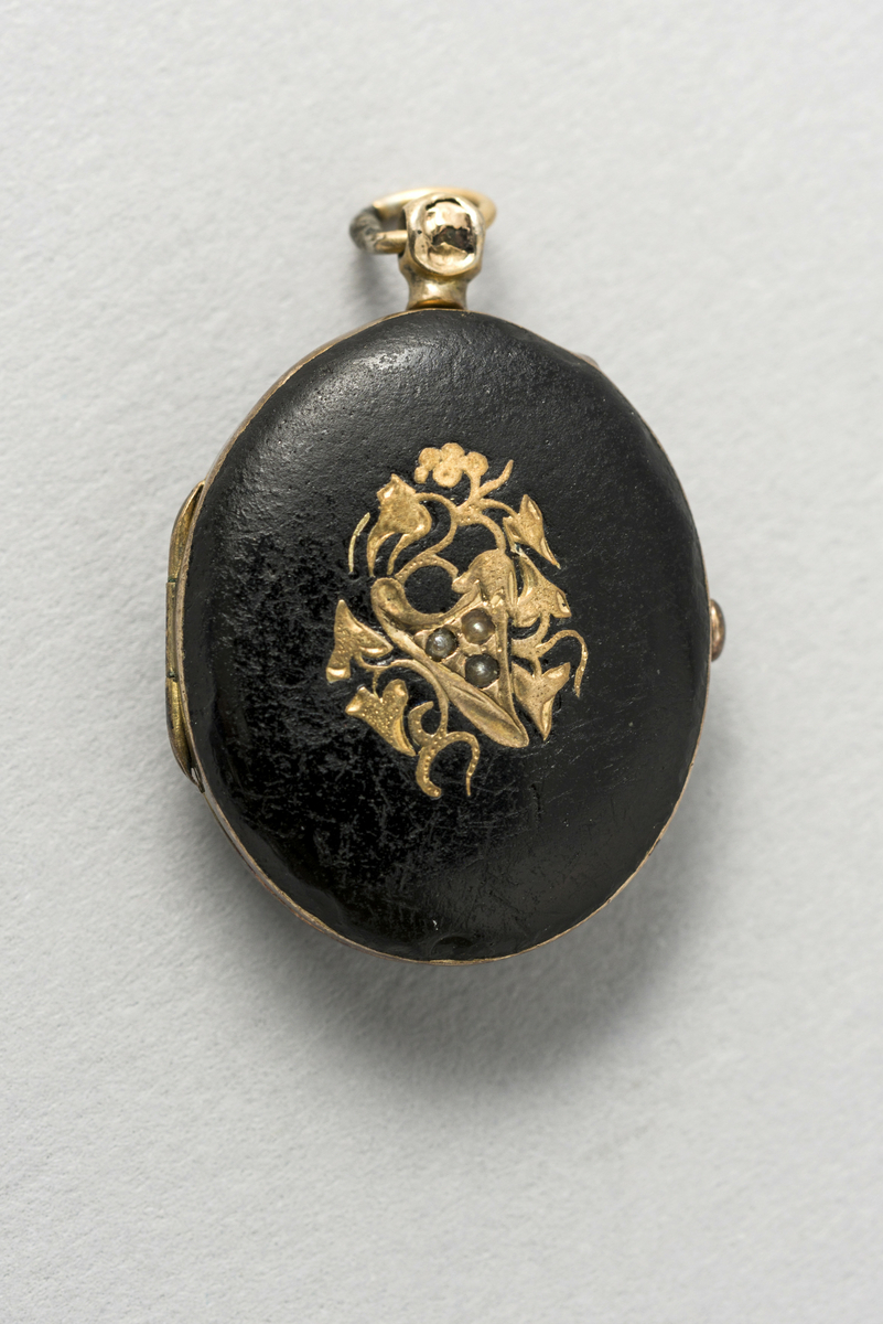 Sort medaljong med floralt mønster på utsiden og fotoportrett av ukjent kvinne på innsiden.