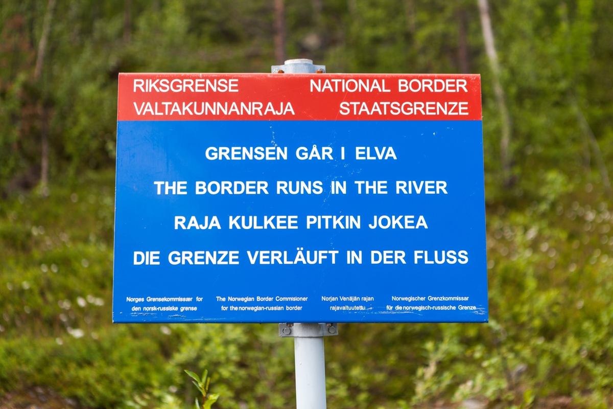 Grenseskilt ved pasvikelva som fortel at grensa mellom Norge og Russland går i elva.