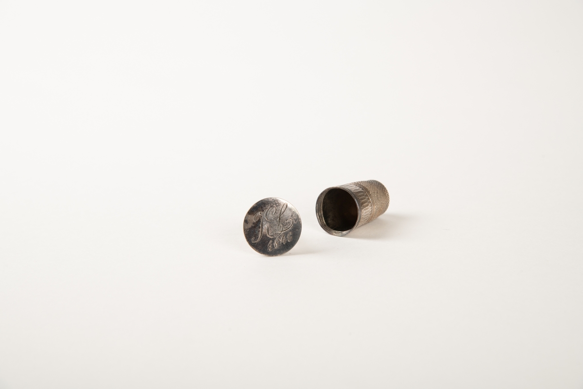 Sidelukket futteral som består av to like deler med profil som et fingerbøl. Foret med hvit silke. I den ene halvdel en fingerbøl av sølv. Inni den en fasettert glassflakong med rester av brunt innhold. Sølvbunn, hvorpå inngravert:  K L 1846.