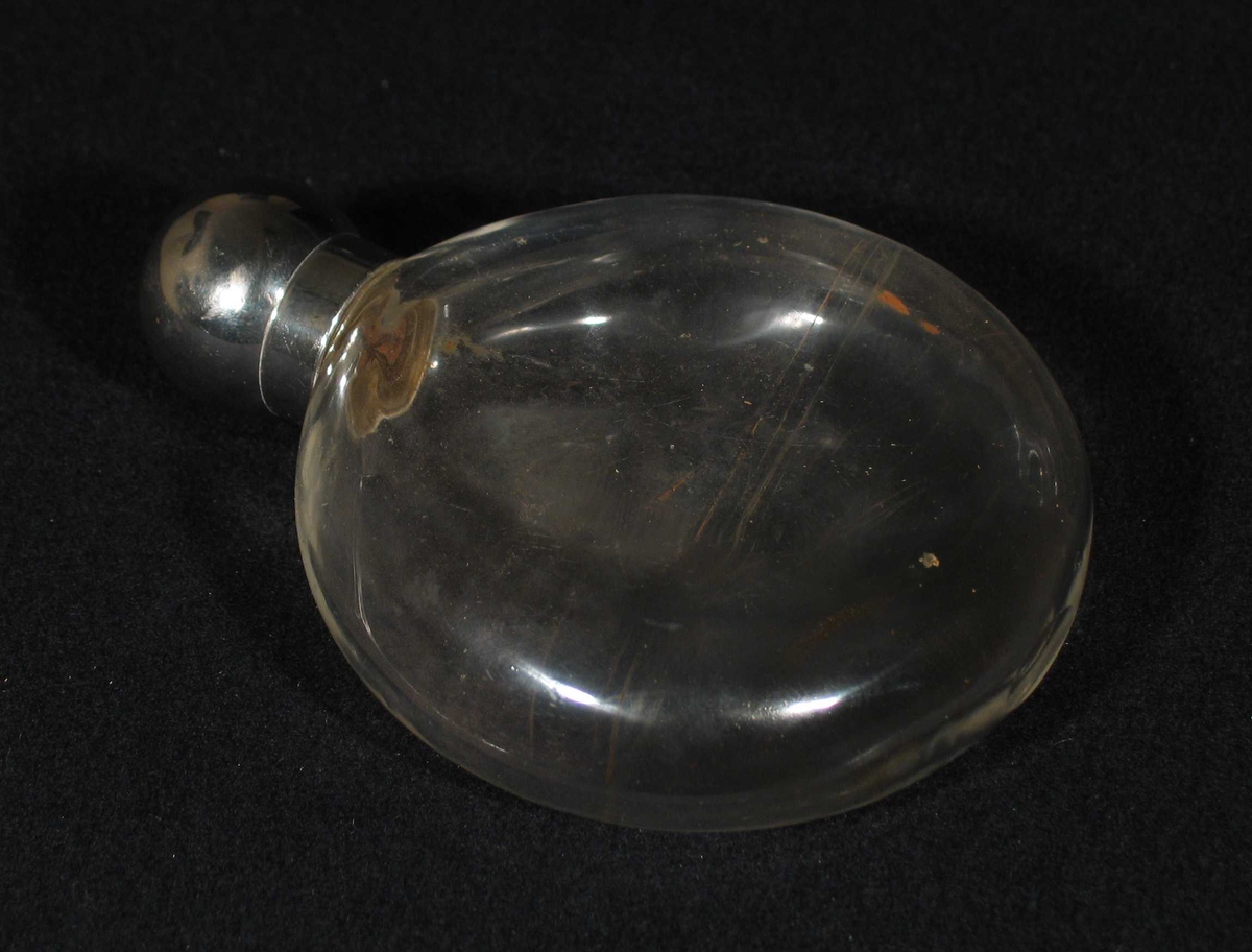 Rund flat flakong i glass. Den har en liten hals og rund metallkork.