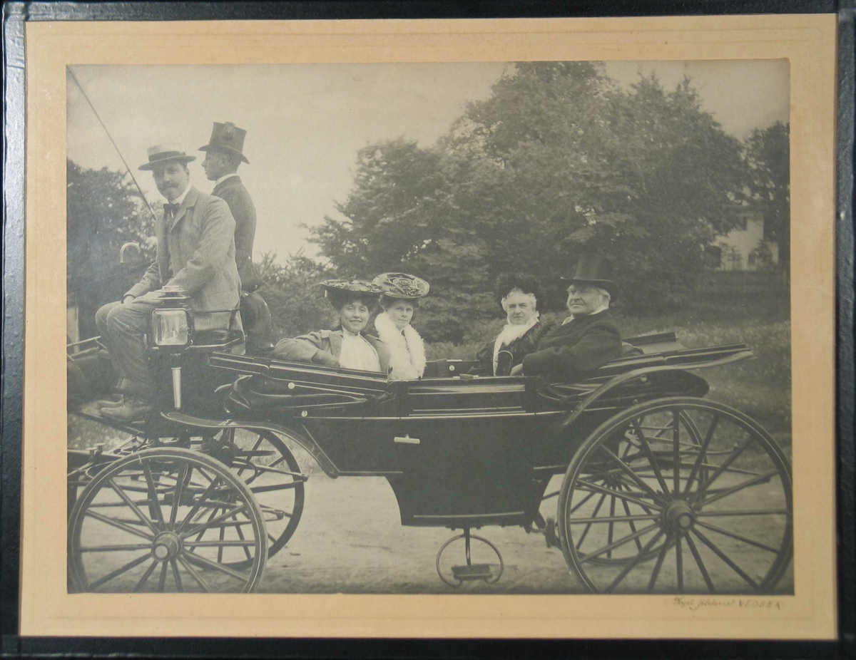 Fire personer anføttes i hestetrukket vogn, to menn på kuskesetet (ene kusk)