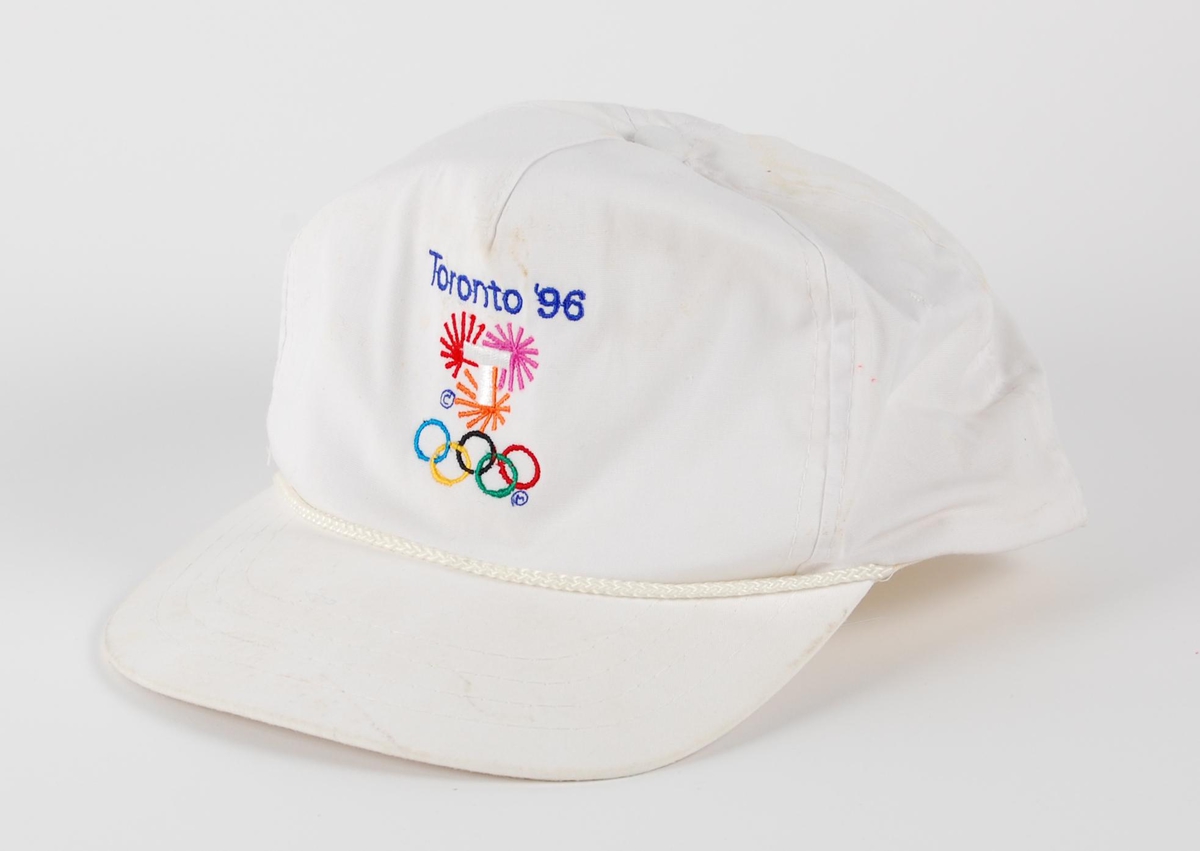 Hvit skyggelue med flerfarget logo for kandidatbyen Toronto i forbindelse med søkerprosessen til de olympiske leker i 1996. Skyggelua har strammespenne av plast.