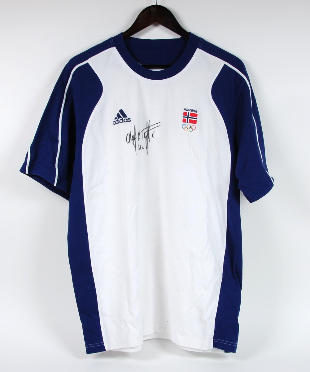 Hvit og blå t-skjorte med laminert logo for Adidas, laminert norsk flagg og signaturen til Olaf K. Tufte.