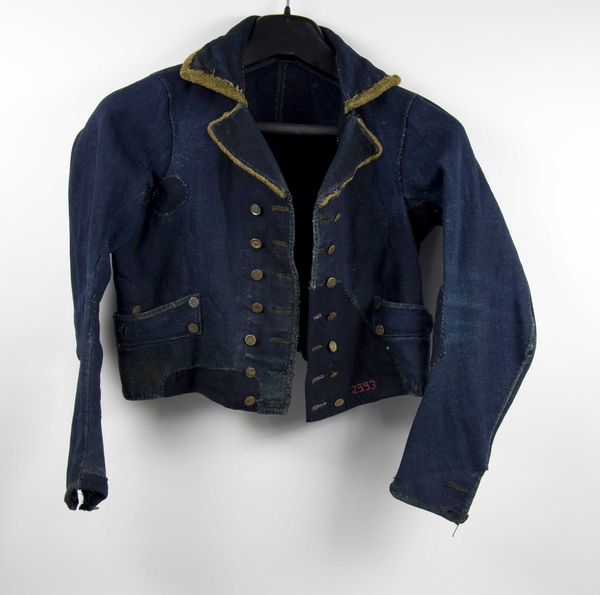 Trøye av kypertvevd vadmel. Ryggsøm og panelsømmer på hver side. Trange ermer. Høy oppstående linningskrage med plass for fire knapper på hver side - to mangler. Kragen har stikninger. Nedbrettet slag. Kragen og slagene er kantet med grønn plysj.
Knapphullsrad og knapperad (7, flere forskjellige motiv) på begge forstykkene slik at trøya kan kneppes både til høyre og venstre. 
Ermesplitt med to knapphull. En knapp mangler på venstre side. Knappene har nok opprinnelig vært festet med skinnsnorer og ullsnorer på vrangen.
En lomme på hvert forstykke, 5 knapper på hver. En lomme mangler fôr, en har ullfôr.
Spor etter fôr (?) på vrangen av forstykkene.  
Trøya har gjennomgått store reparasjoner.
