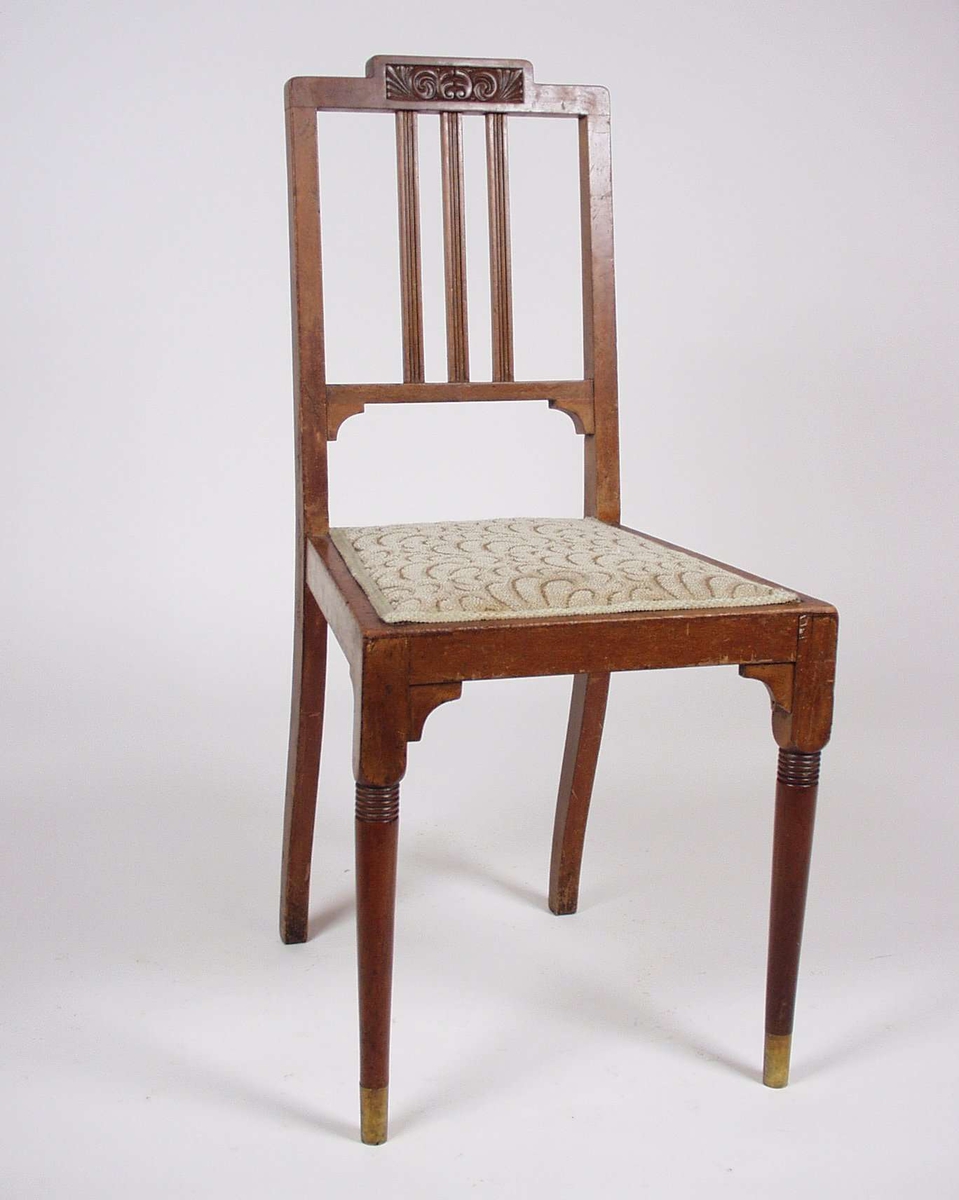 Stolen er av tre med mønstret tekstiltrekk. Toppstykket er utskåret og forbeina er utskåret.