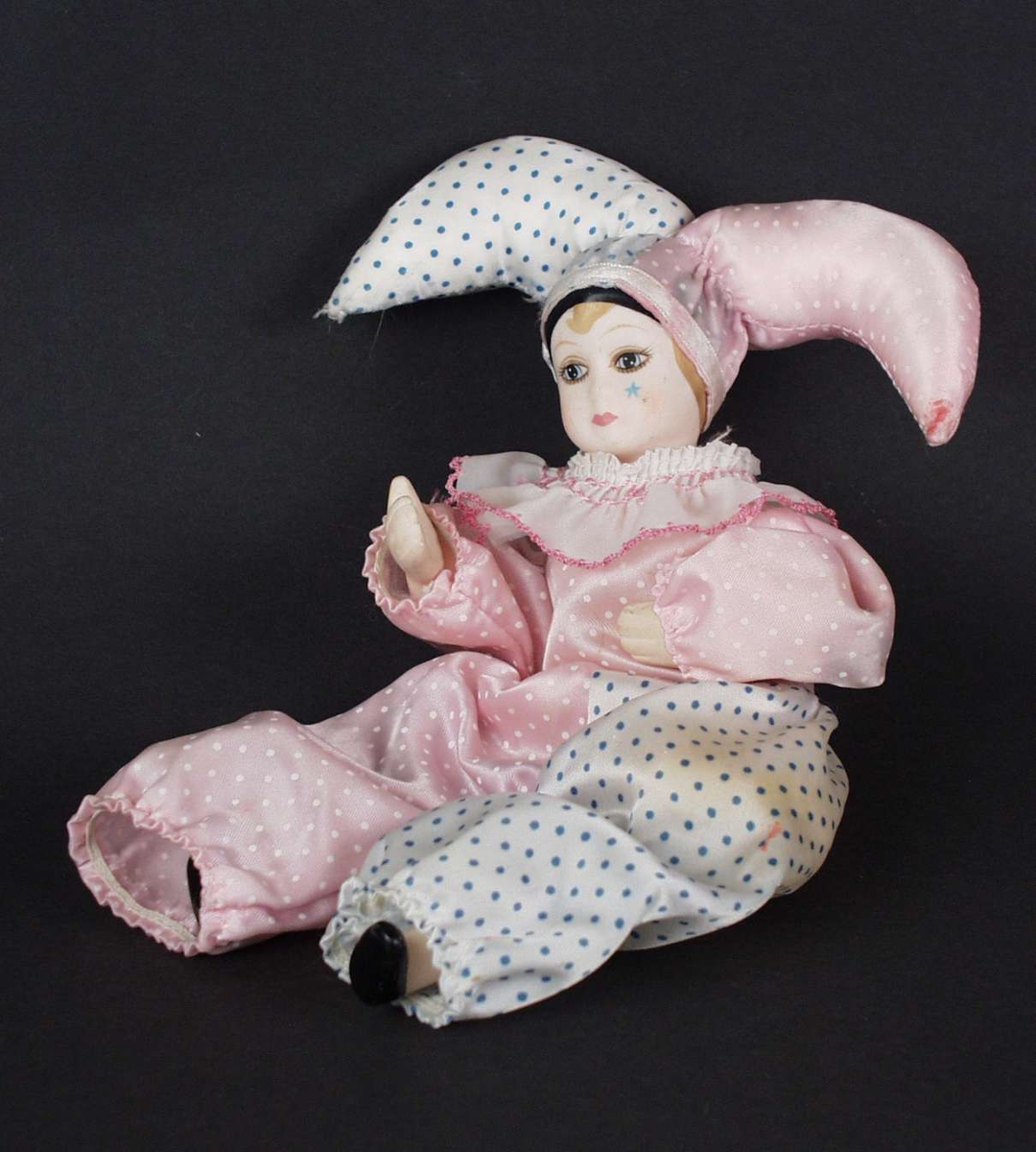 Dukke med hode, hender og bein i keramikk. Den har klovneklær i rosa og hvitt.