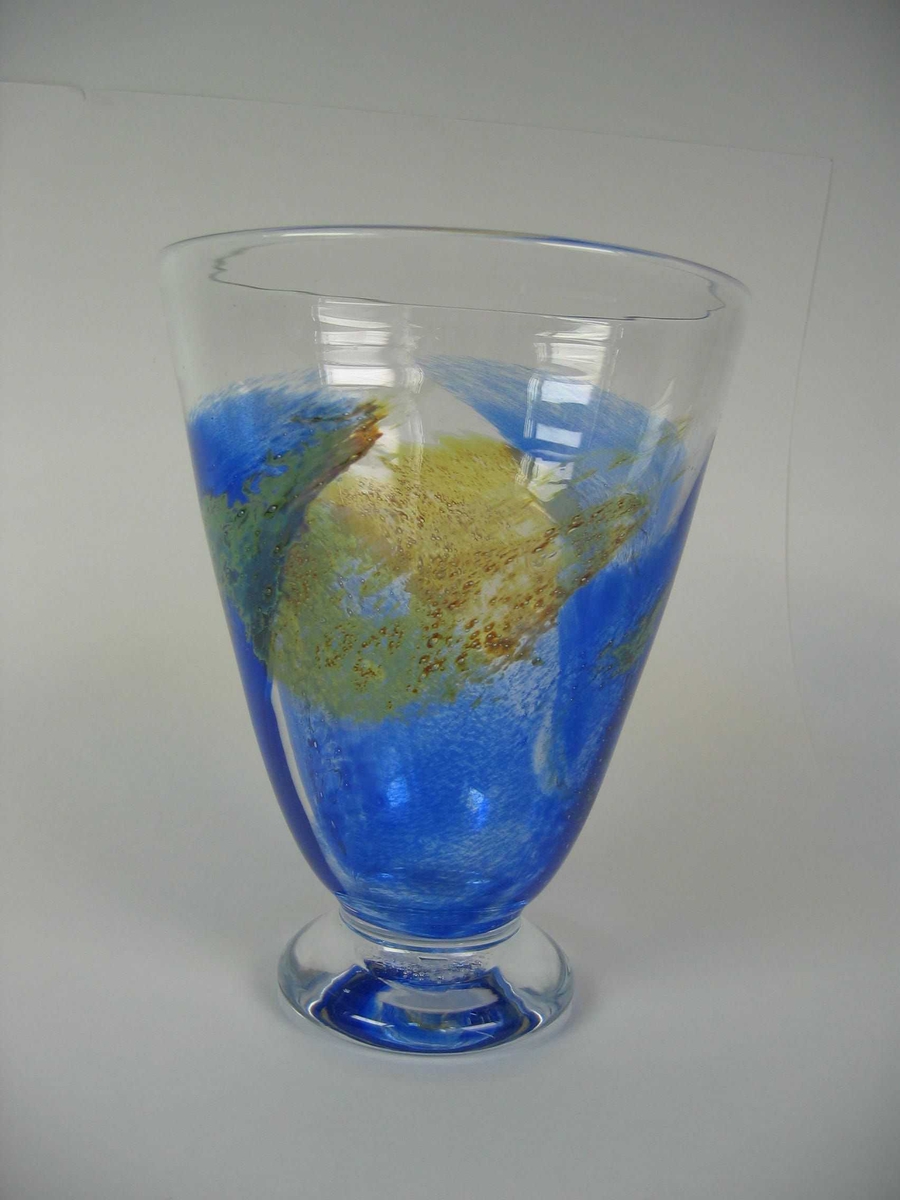 Lett flatklemt konisk formet vase på en liten fotplate. Blåst i to deler. Hovedfargen er klart glass, med noe blått og brunspettet.