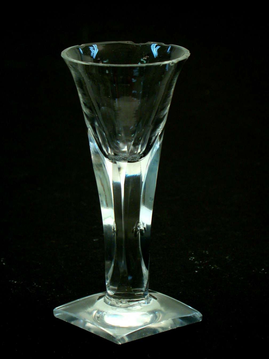 Glasset er et spissglass med firkantet fot. Stetten er fasettslipt slik at den blir firkantet. Det er hakk i randen på klokken og på foten. 