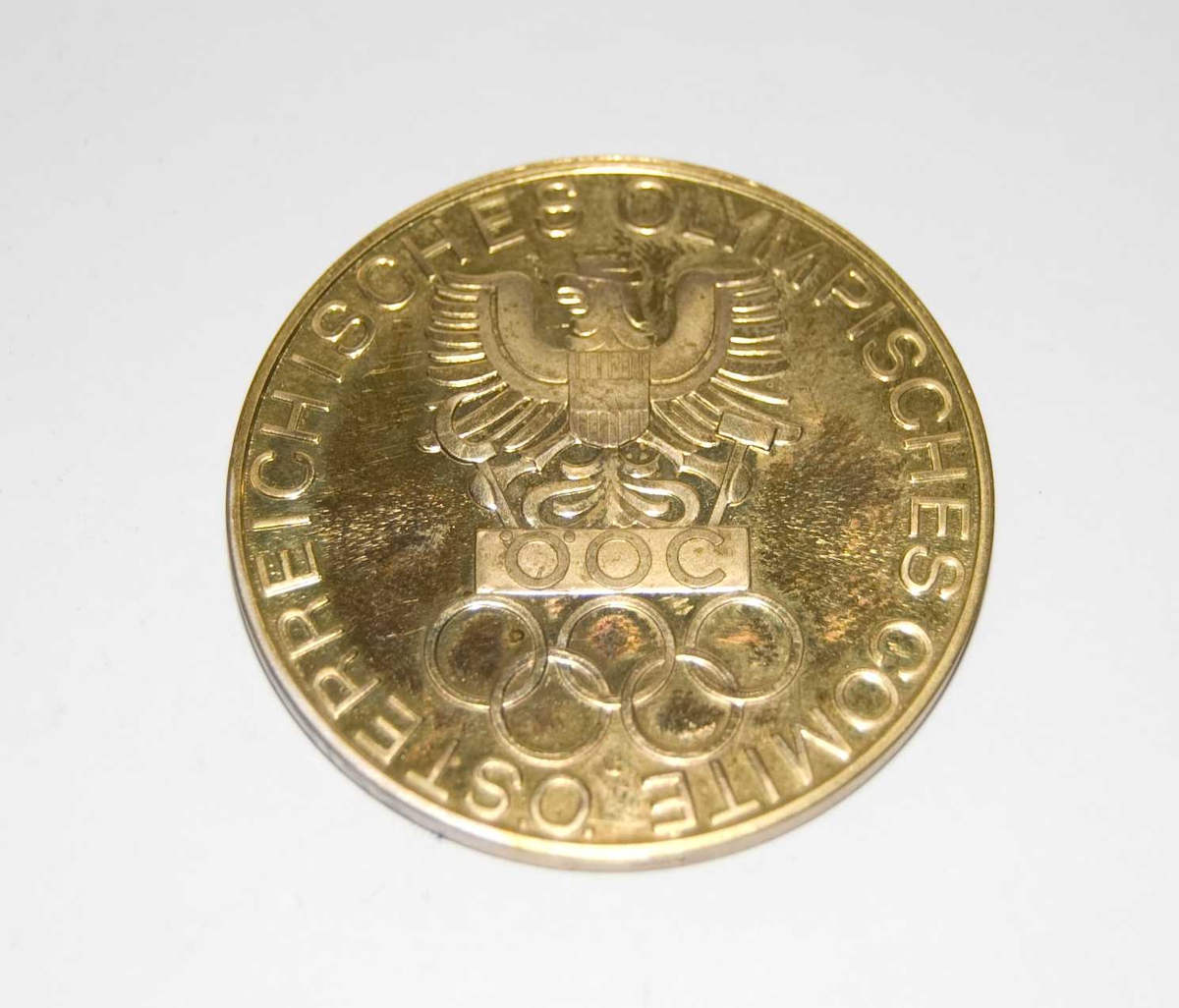 Gullfarget medalje med motiv av Østerrikes riksvåpen og de olympiske ringene. Det følger med et blått etui med samme motiv som medaljen.