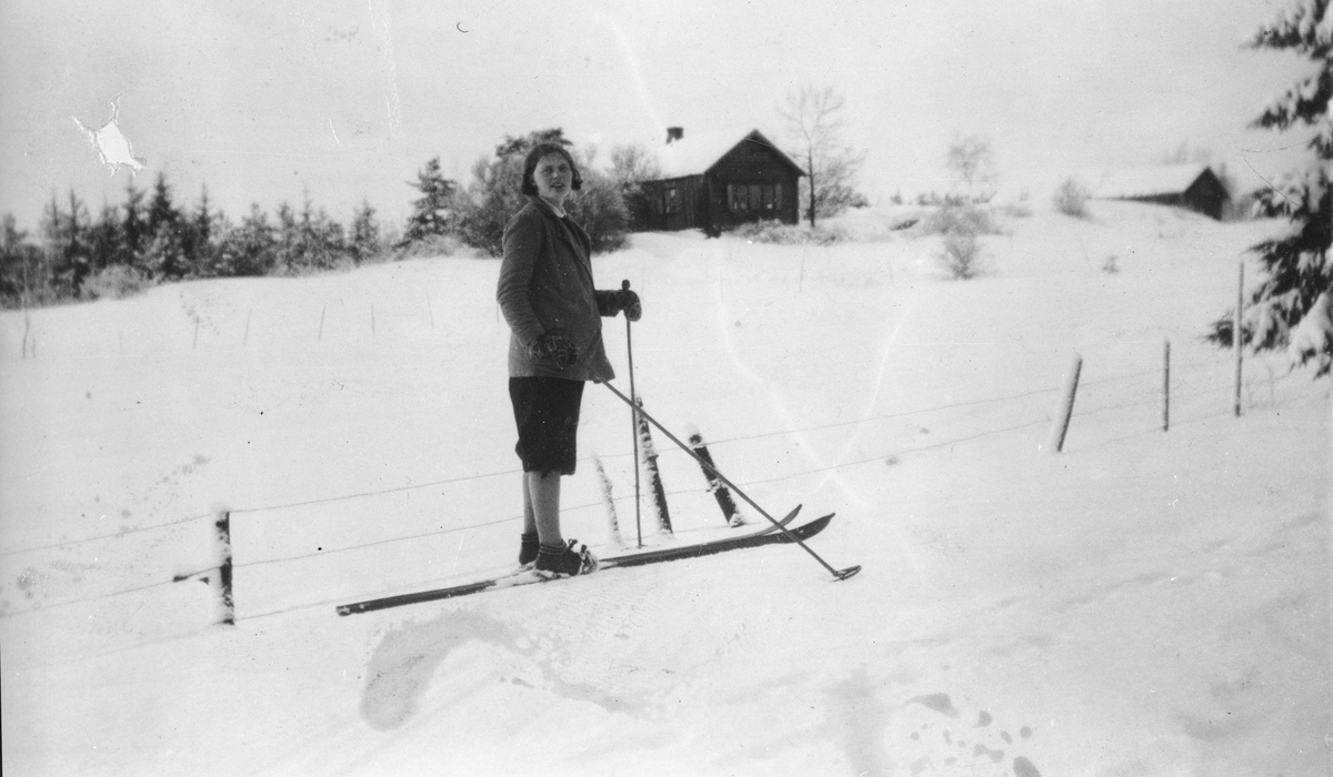 En kvinne på ski foran småbruket Høyås.