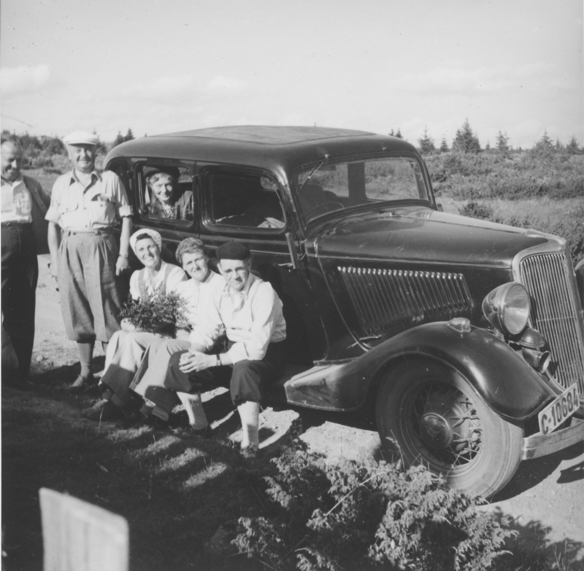 En gruppe mennesker foran bil (Ford 1934).