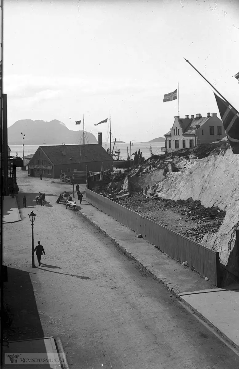 I bakgrunnen er Skansekaia og lengst bak ser vi Godøya..Til høyre "Strømsheims Hotell" i halv utgave...Forskjellen ser dere på bildet fra 1934 som viser det i hel utgave. Da var navnet Hotell "Hospitset"..Det flagges på halv stang ,så kanskje er det Ibsens død ?.