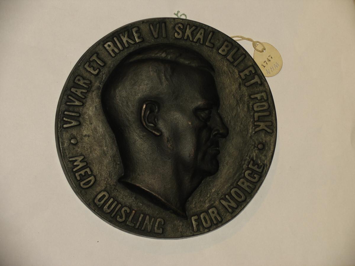 I bronse 23 cm i diam av Quisling med innskrift rundt : Vi var et rike Vi skal bli et folk med Quisling for Norge : I relieff.  Deponert FMU/Nordenfjeldske Hjemmefrontmuseum.