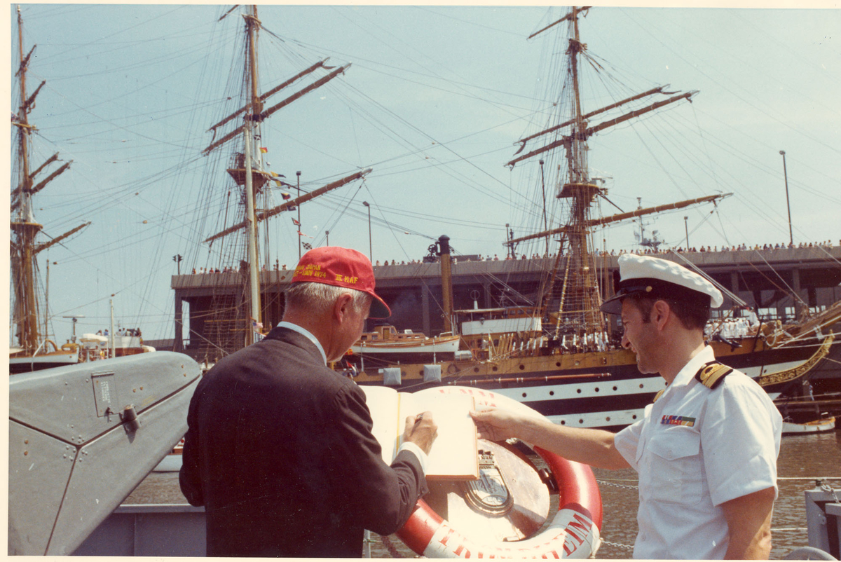 Oslo-kl.- fregatt KNM "Trondheim" får besøk av Secretary of the Navy J. W. Middeldorf i New York, sommeren 1976. Mr. Middeldorf signerer i offisersmessens gjestebok. I bakgrunnen det italienske skoleskipet Amerigo Vespucci.