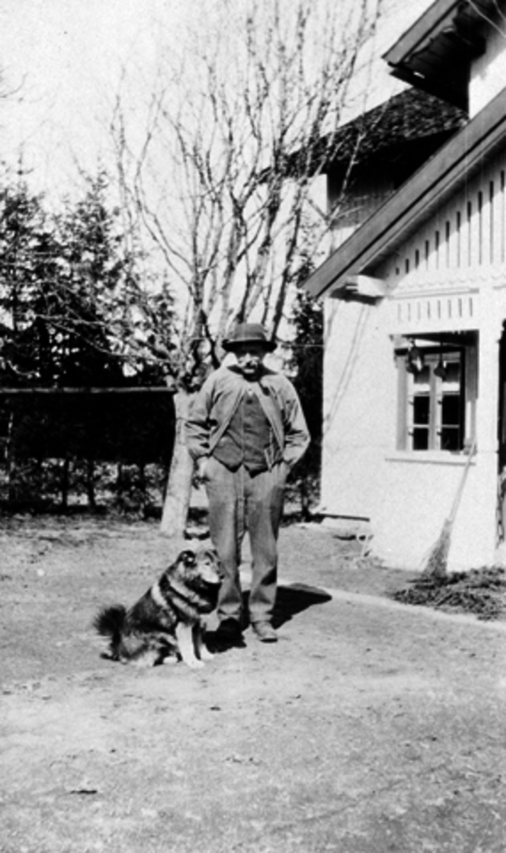 Mann og hund utenfor hus på Kylstad gård, Furnes, Ringsaker.