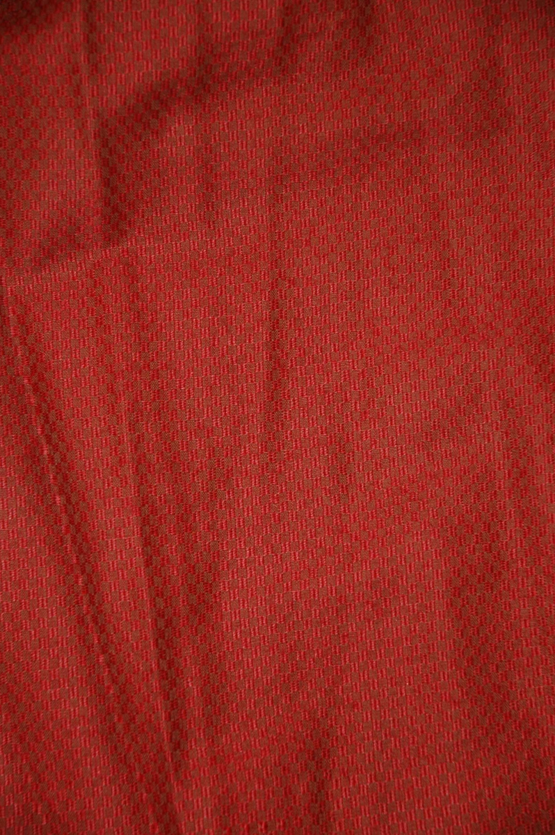 Smårutete, rødt halvull skjørt som er delvis foret. Skjørtet har burgunderrødt  kantebånd nederst. Lomme i ene sida.
