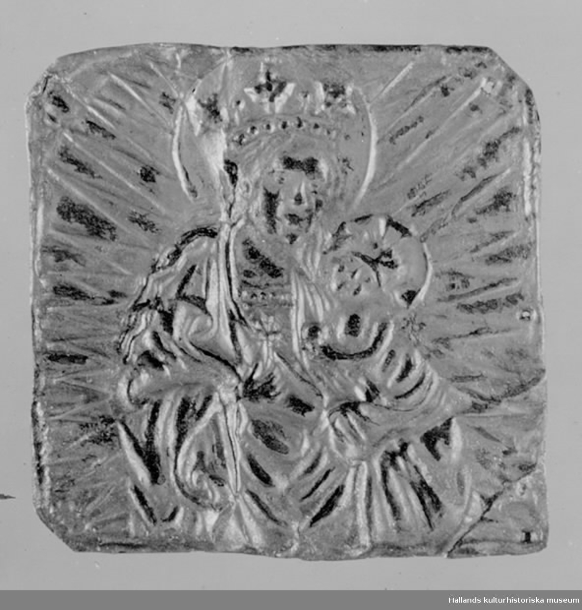 Förgylld kopparplåt med pressad bild av madonnan och barnet omgiven av en strålgloria. Tre hål i plåtens högra sida.