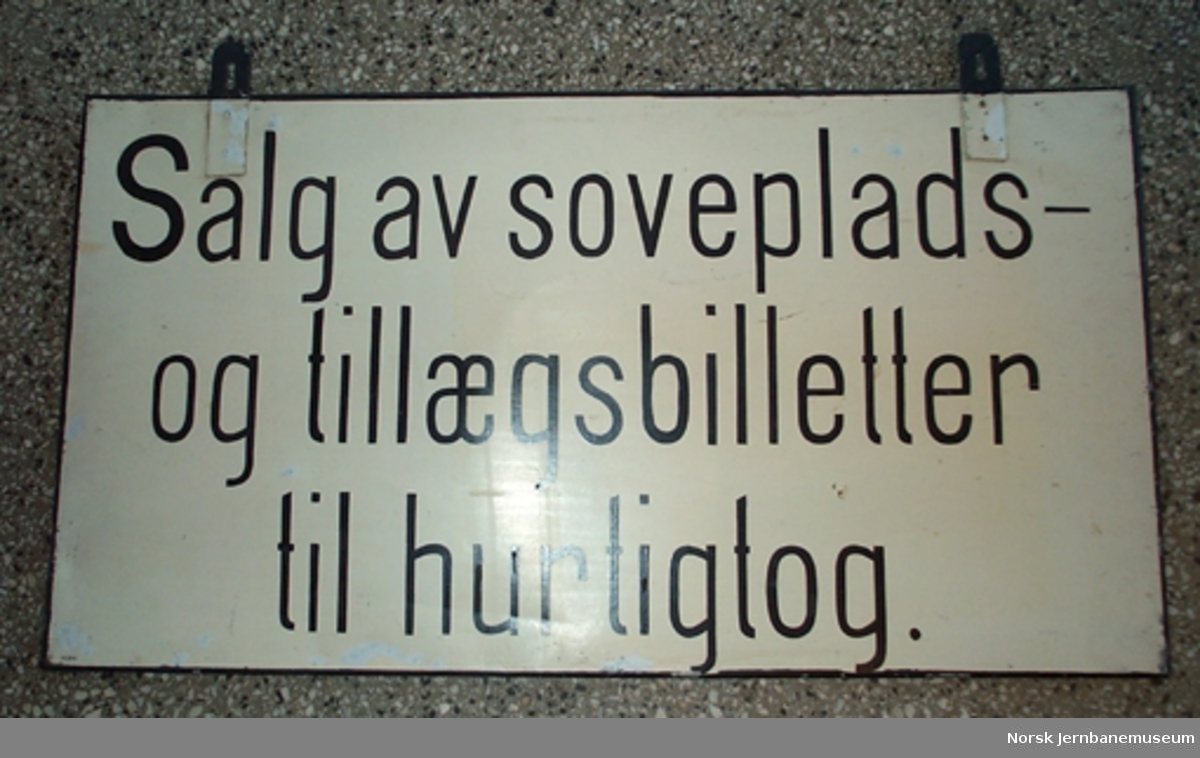 Skilt tosidig "Salg av billetter til Eidsvold-Ottabanen Hovedbanen og banerne over Kristiania" og på baksiden "Salg av soveplads- og tilægsbilletter til hurtigtog"