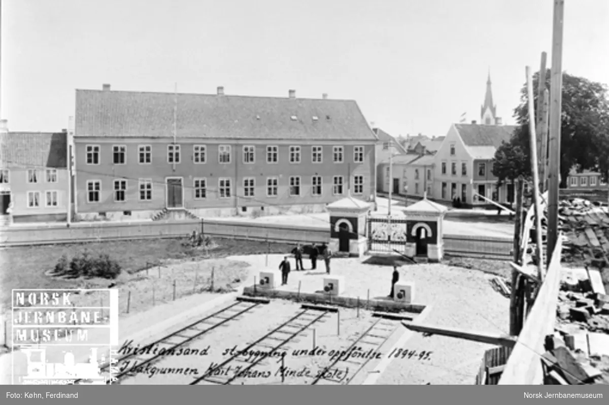 Kristiansand stasjonstomt med stoppbukkene i spor 1-3 og porten mot byen, i bildekanten ser stasjonsbygningen under oppførelse