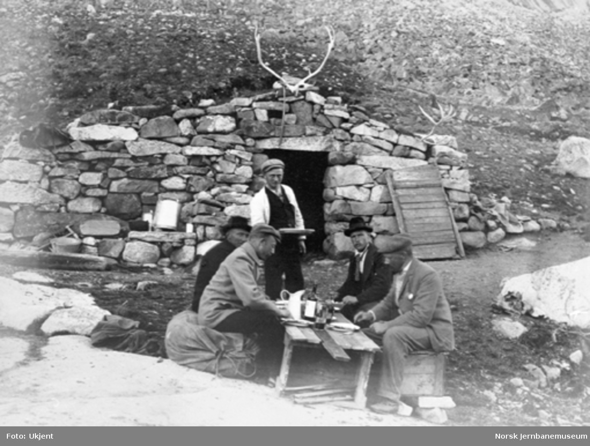 Bergensbanens anlegg; stikkingspersonale spiser middag utenfor ei steinbu ved Oksebotn