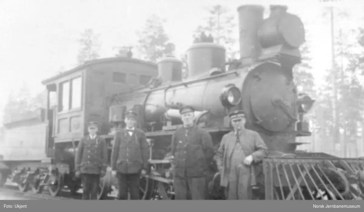 Damplokomotiv type XXIIId nr. 77 foran kistog på Elverum stasjon; togpersonalet poserer i forgrunnen