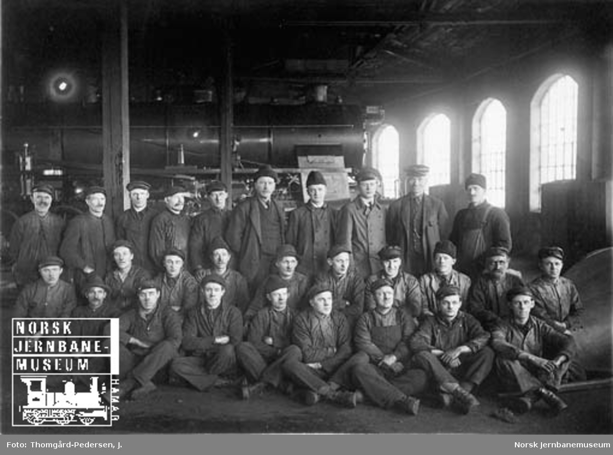 Gruppebilde av lokomotivfolk i Hamar lokomotivstall (ringstallen) med nyleverte damplokomotiv nr. 446 i bakgrunnen