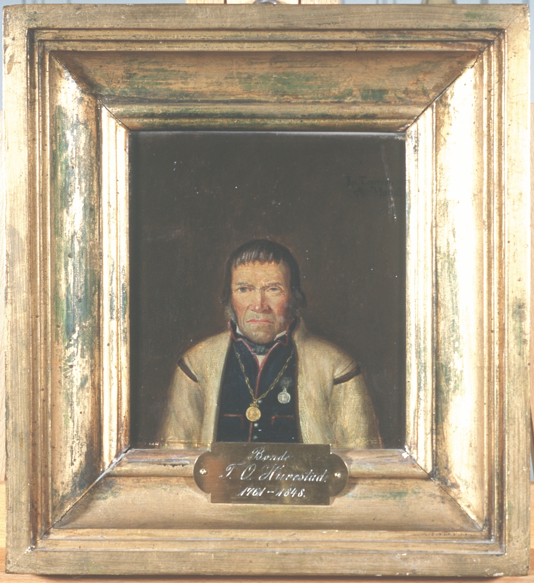 Portrett av Tallev O. Huvestad. Hvit trøye (jakke) og mørk vest m/røde kanter. 
Frederik VI's erindringsmedalje i kjede om halsen, Danebrog eller Borgerdådsmedaljen på brystet.