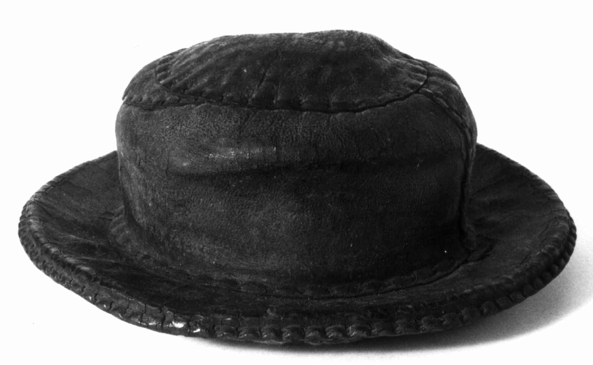 Rund hatt med brem. Sydd med lærbånd. Toppen av hatten er laget med to mindre biter av lær, antakelig en reparasjon. Foret er laget av tovede fibre.