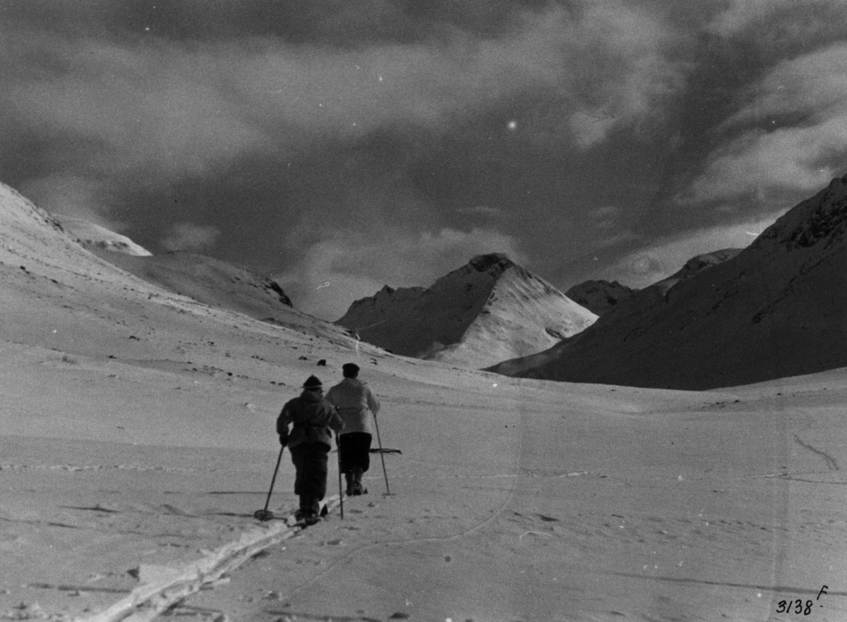 Skiløpere i Uladalen i Jotunheimen med snødekte fjell og sol.