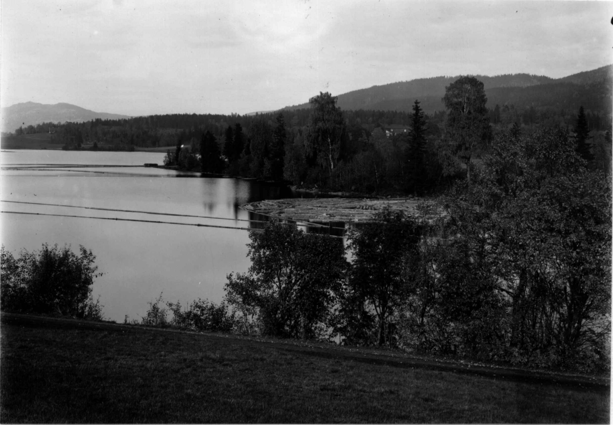 Bogstadvannet, Oslo 1908-10. Oversiktsbilde. Tømmer på vannet. Skog.
Bebyggelse i bakgrunnen. 