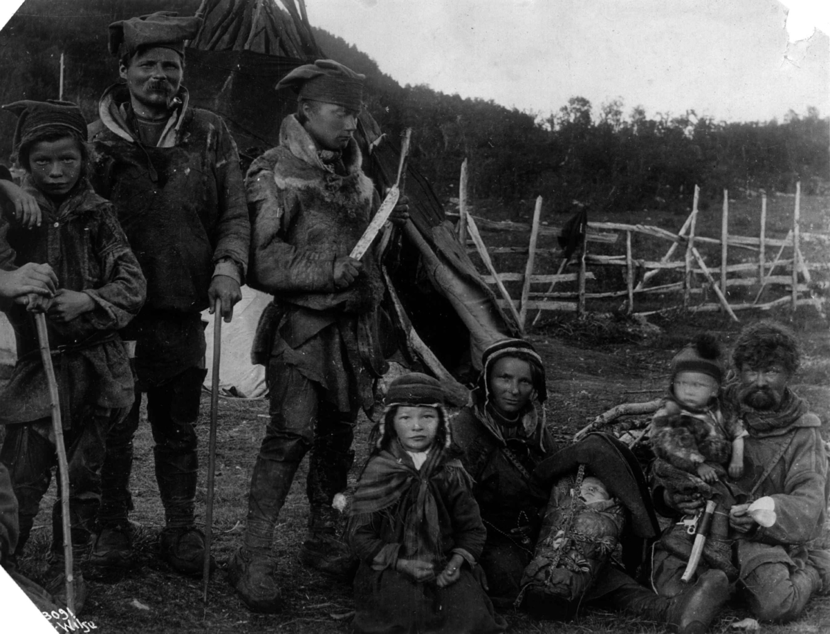 Svenske samedrakter. En kvinne med barn i komse, menn og barn samlet utenfor et telt. 1911