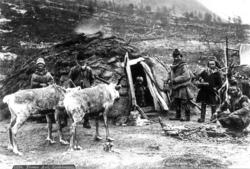 Svenske samer foran gamme, to reinsdyr i forgrunnen. Muligen