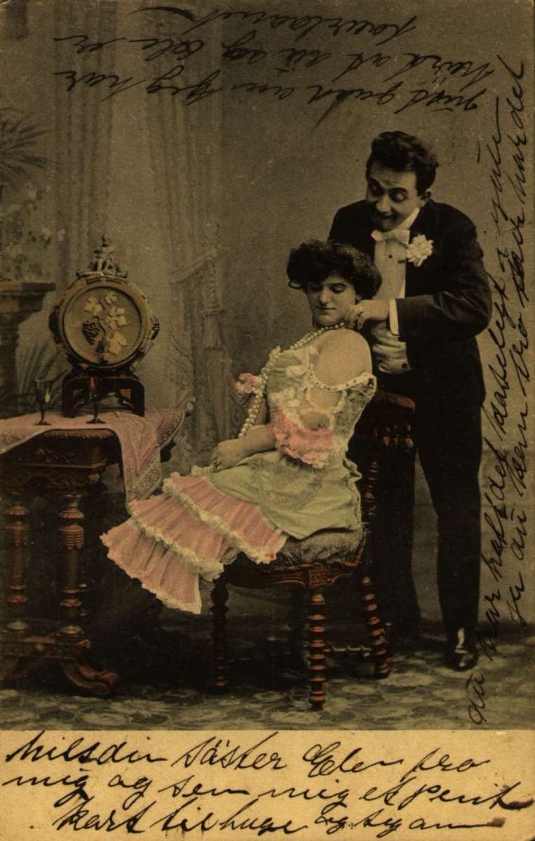Postkort, Nyttårshilsen. Fotografisk. Kolorert. Mann gir kvinne et halsbånd. Stemplet 30.12.1906.