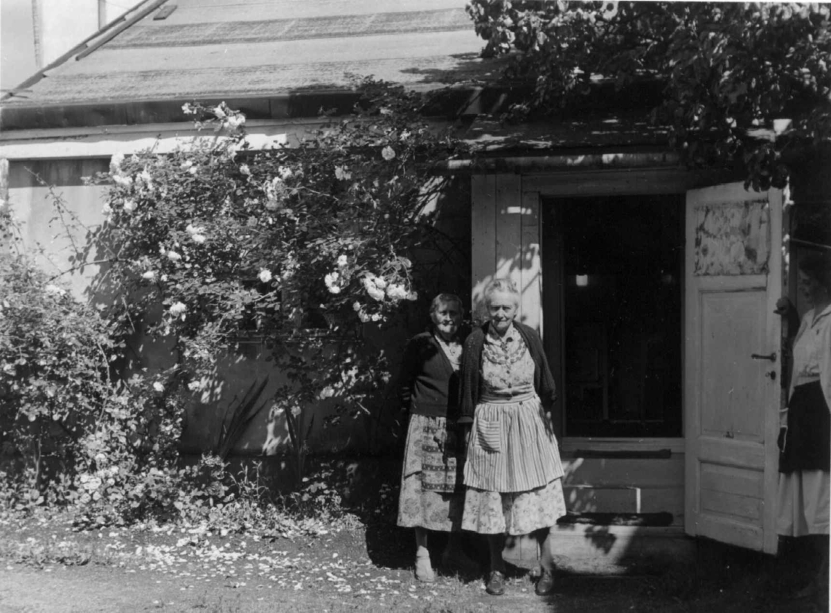 Enerhaugen, Oslo 1958. To kvinner foran lavt hus med åpen inngangsdør.