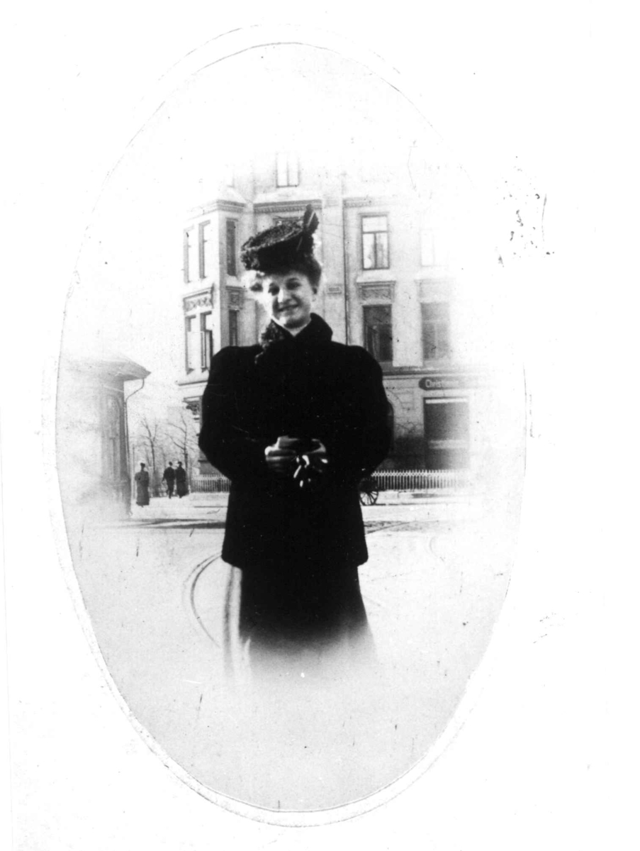 Fotografi av kvinne med svart pels og hatt stående i bygate.