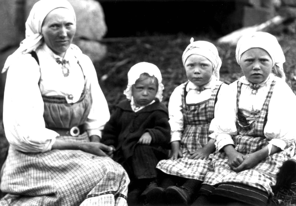 Kvinne- og barnedrakt, gruppeportrett, Valle, Setesdal, Aust-Agder, antatt 1924. Kvinne med tre barn sittende utendørs. Fra "De Schreinerske samlinger" (skal oppgis).