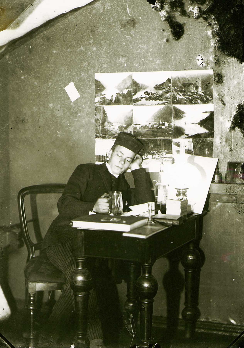 Portrett av mann i hatt og dress i interiør, ant. fotograf  Thorvald Aron Brunskow (1871-96), den yngste av de to Brødrene Brunskow. Ant. i deres atelier, Oslo, med bord, stol, oppklebede landskapsfotografier på veggen og ølglass i hånden.
