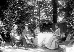 Familiegruppe i hageselskap med dekket kaffebord. Sigrid f. 