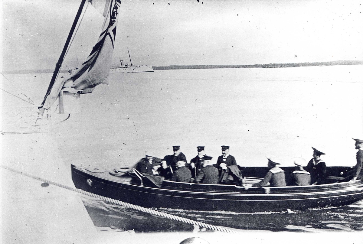 Fra Molde havn, Møre og Romsdal. Uniformskledde menn ombord i motorbåt, akter av en annen båt med flagg og skip lenger ute.