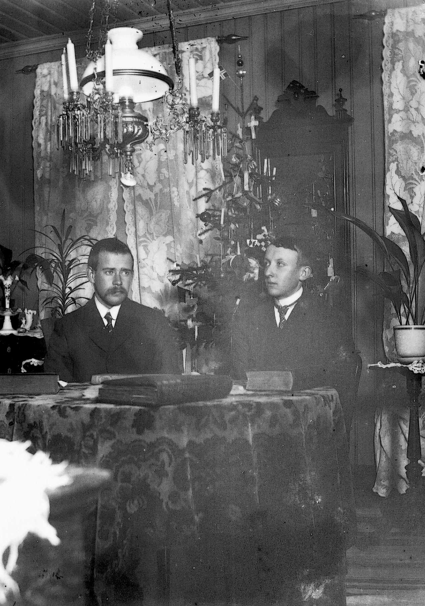 To mannlige gjester på besøk i leiligheten i Oslo - stueinteriør med rundt bord, speil og lysekrone.