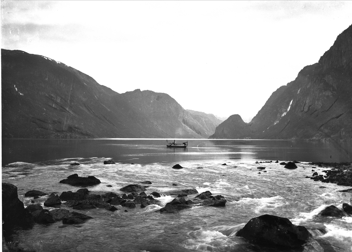 Landskapsfotografi fra Odda i Hardanger.Antakelig Sørfjorden med fiskeskute. I forgrunnen elveutløp.