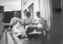 Tre kvinner sitter på en veranda og broderer og prater. Robs