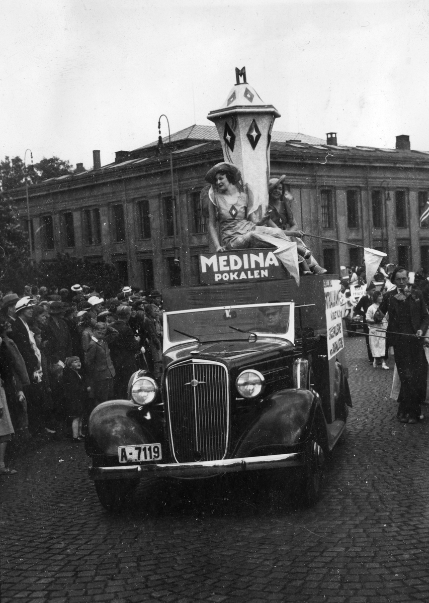 Oslodagen 1/6 1935. Reklame for Medina sigaretter. To kvinner i kjoler pyntet med logotypen for Medina sigaretter sitter på taket til en bil sammen med en stor Medinapokale.