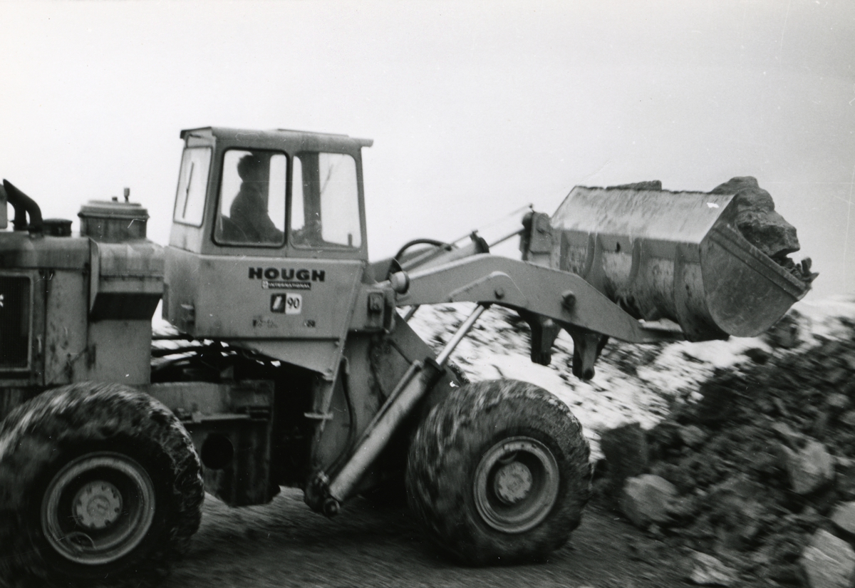 Byggeplass.
Konstruksjon av Tiedemanns Tobaksfabrik på Hovin i 1967. En gravemaskin av merket Hough i arbeid på byggeplassen.