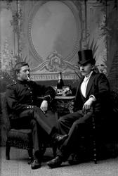 Gruppeportrett, to menn sittende ved bord, champagne og siga