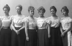 Gruppeportrett, syv kvinner i hvite kortermede bluser og sva