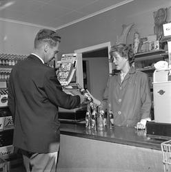 Mandal, 06.09.1964. Butikkinteriør, mann handler ølflasker f