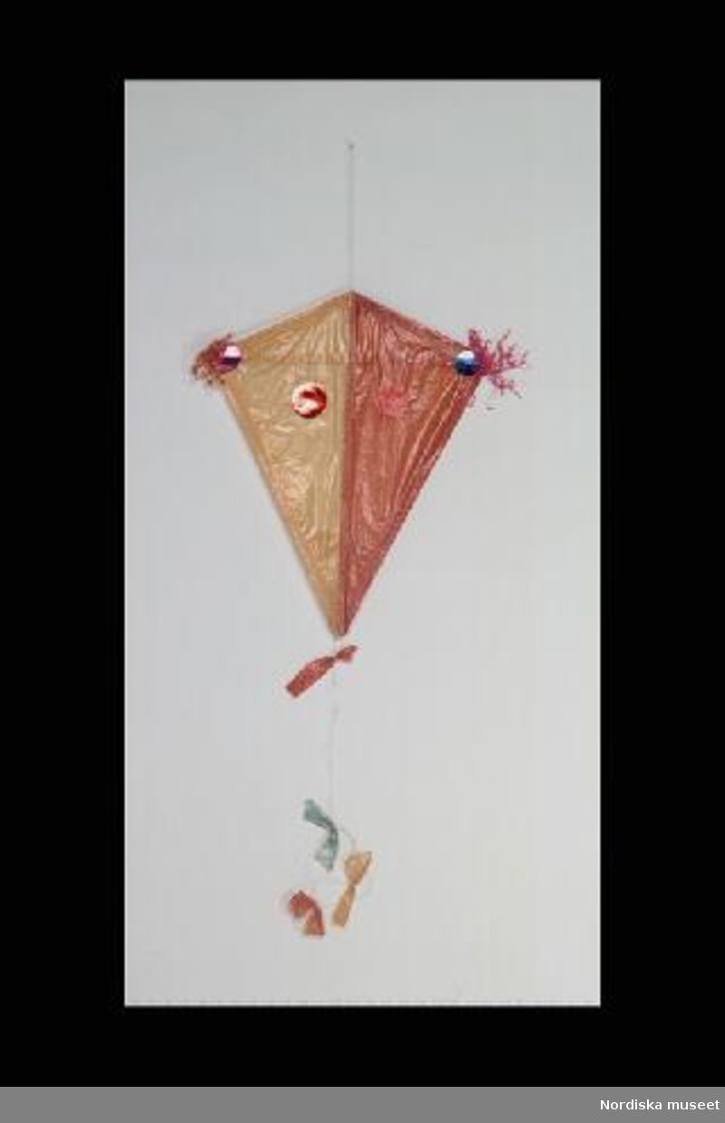 Inventering Sesam 1996-1999:
L 45    B 35  cm
Leksaksdrake, stomme av trä, gult och rött papper med prickar av rött och blått glanspapper. Papperstofsar i rött och lila. Svans av snöre med rosetter i rött, grönt och gult. 
AR 1961
Birgitta Martinius 1998